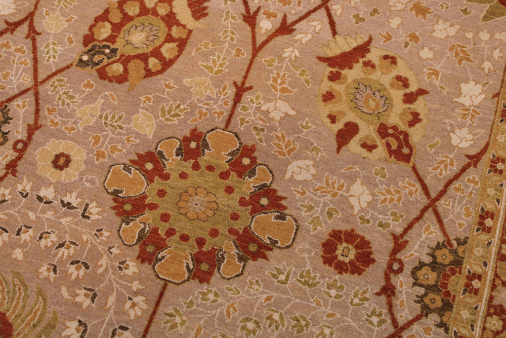 A close-up of a traditional patterned rug featuring large floral medallions and delicate leafy vines in rust red, beige, ochre yellow, and muted green on a dusty pink background.